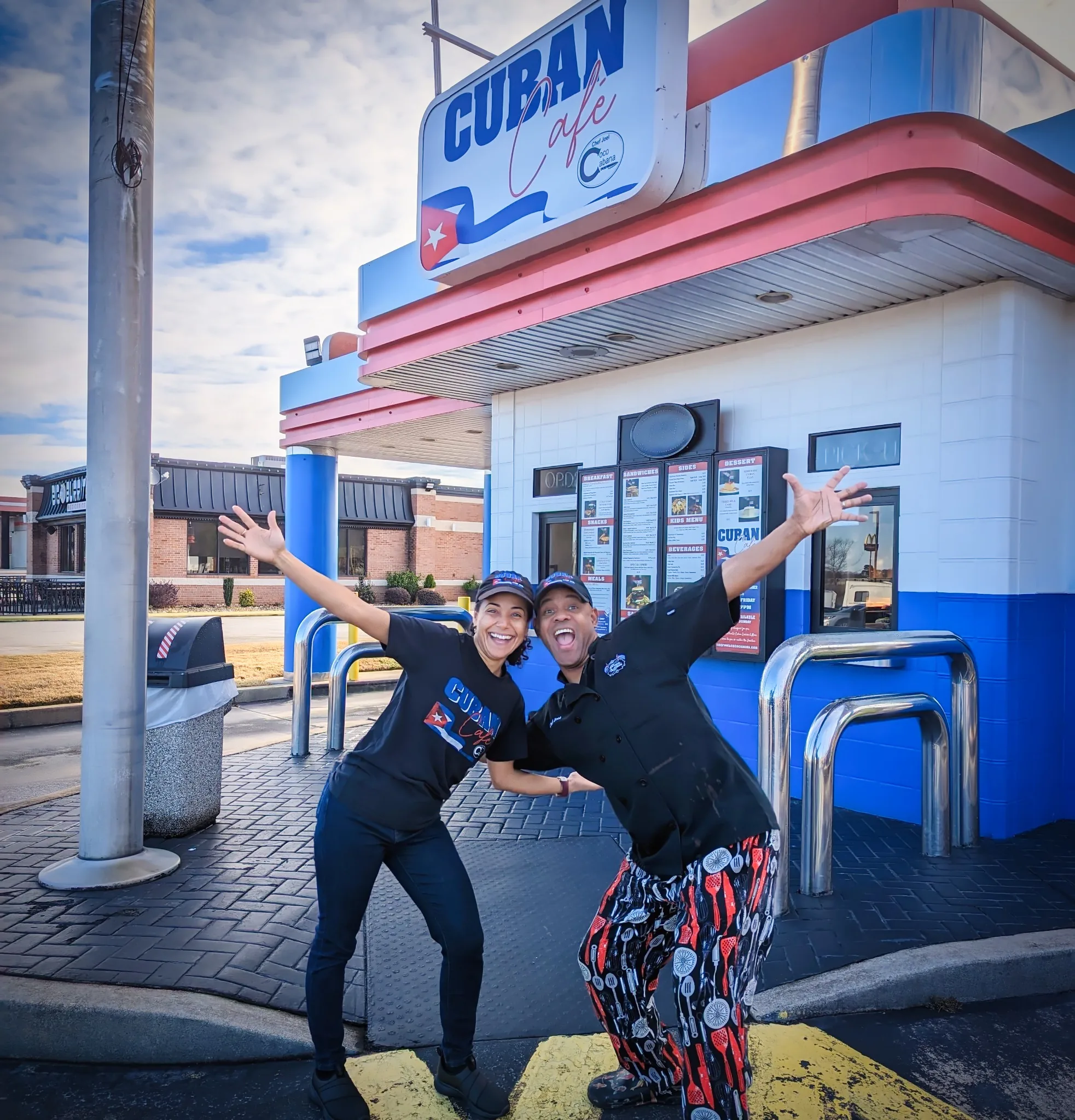 Yinet and Chef Joel with arms wide open in front of the Cuban Café drive-thru