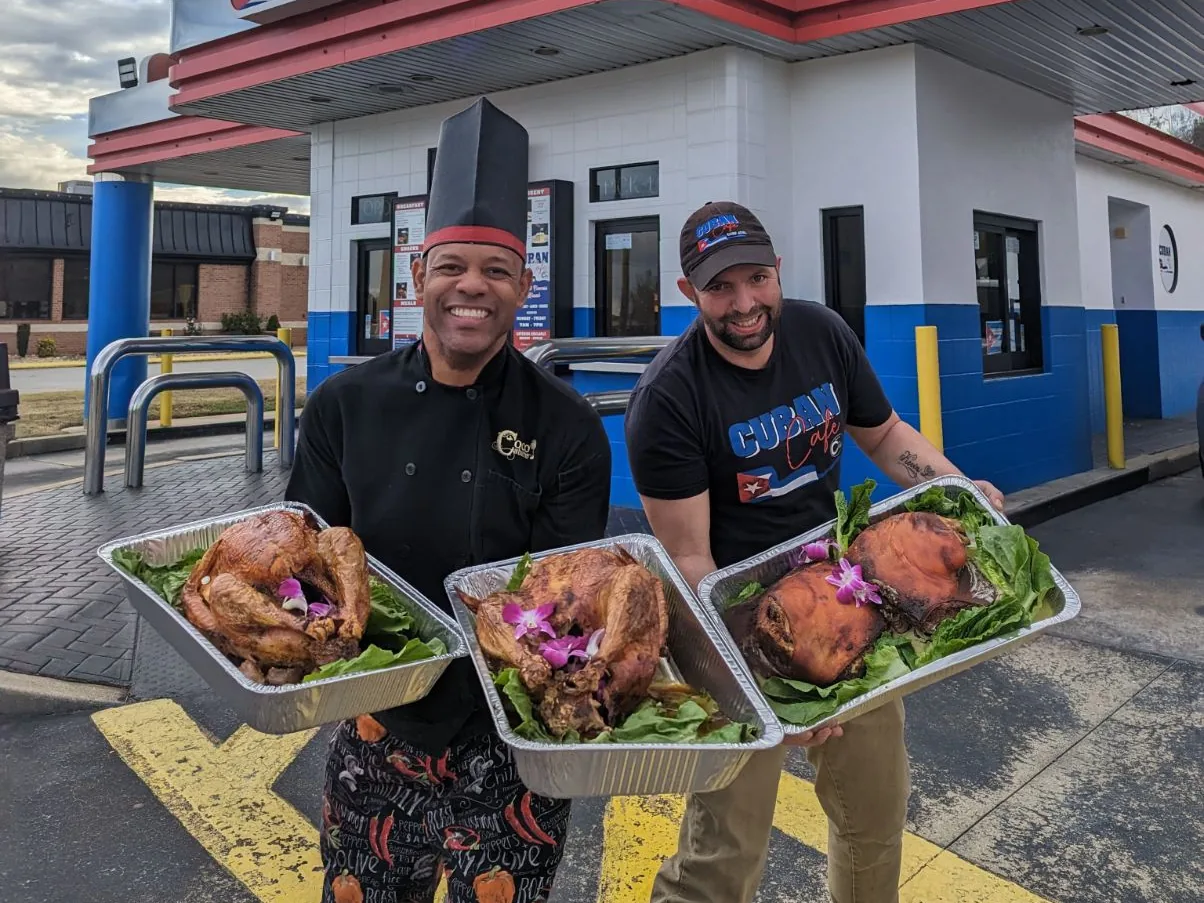 Chef Joel and a teammate holding fresh-roasted Cuban-style turkeys and roast pork outside the Cuban Café