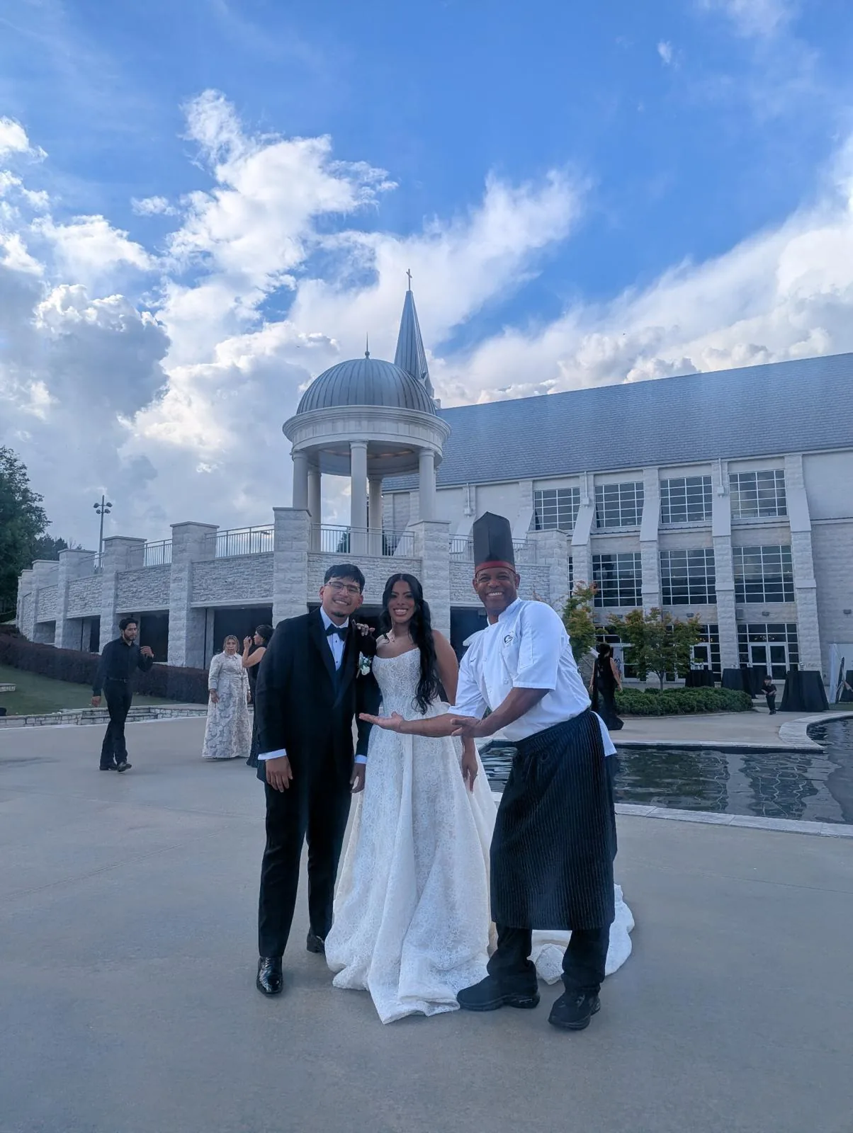 A bride and groom with Chef Joel outside a wedding chapel